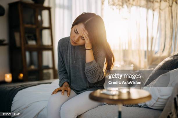 young asian woman sitting on the bed feeling sick and suffering from headache, a glass of water and medicine on the side table - tontura imagens e fotografias de stock
