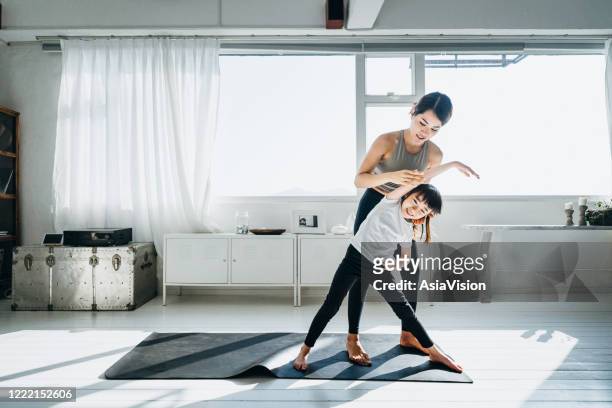 Joyful young Asian mother and little daughter exercising and practising yoga together at home