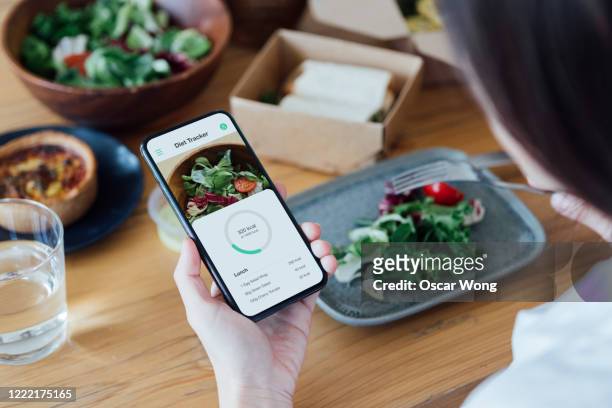 young woman counting calories with smartphone while eating - tipo di cibo foto e immagini stock