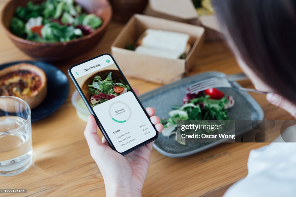 Young Woman Counting Calories With Smartphone While Eating