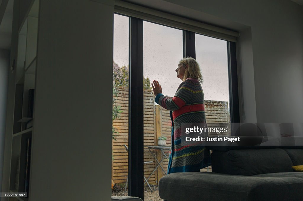 Senior woman looking through wet window