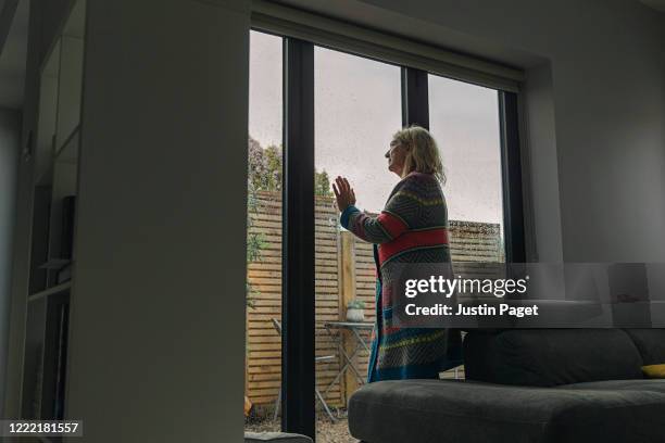 senior woman looking through wet window - glass door stock pictures, royalty-free photos & images