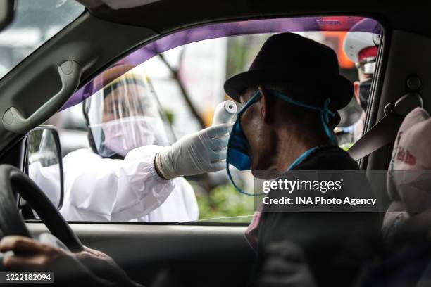 Medical worker checking road users body temperature as a measure prevent COVID-19 during the implementation of the large-scale social restrictions at...