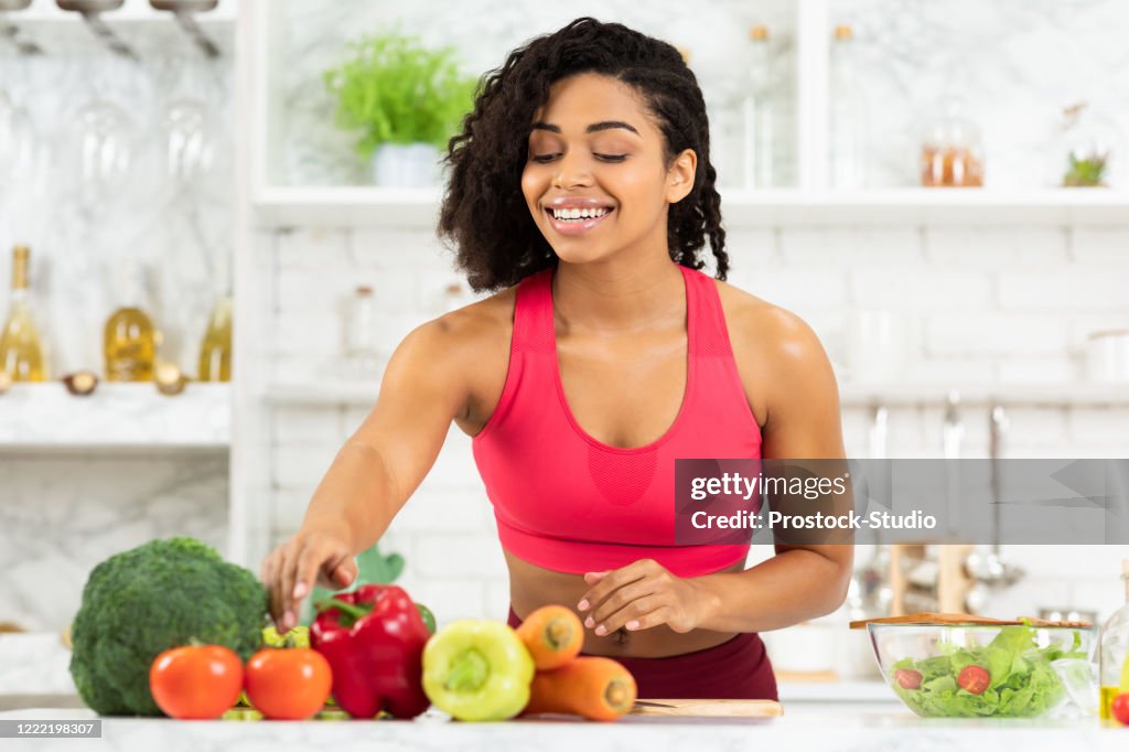 Happy young black woman preparing vegetable salad