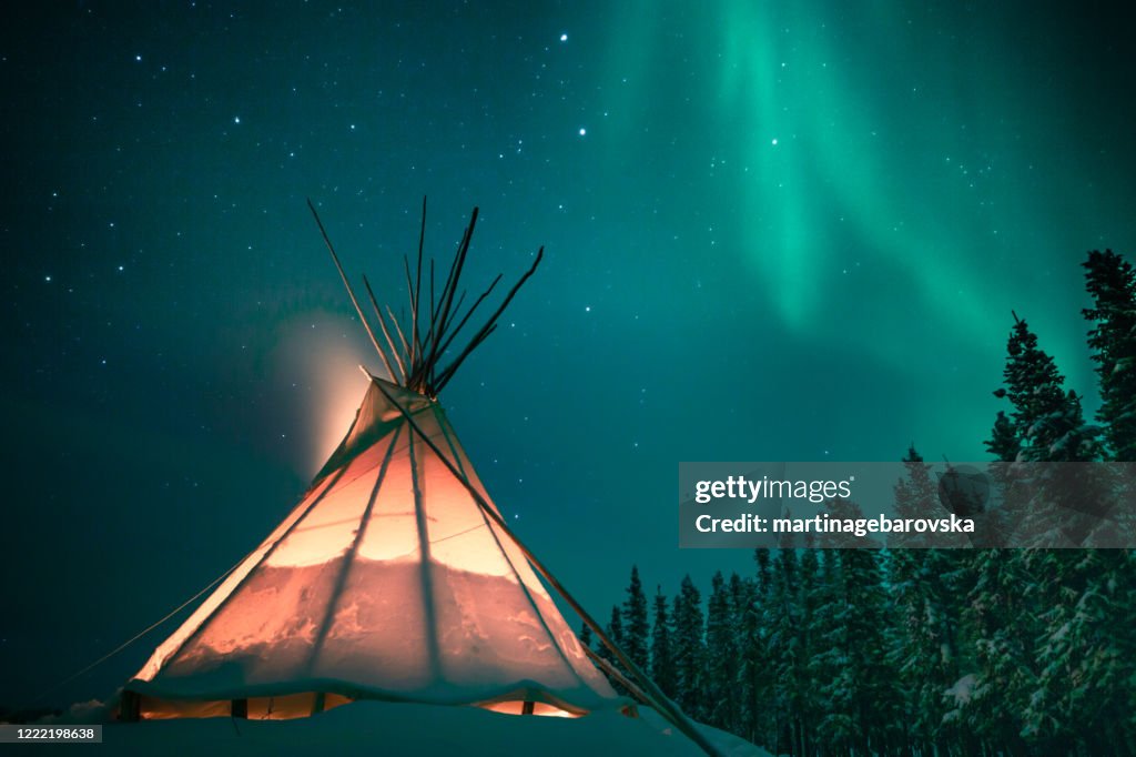 Glowing teepee in the snowy forest under the northern lights, Yellowknife, Northwest Territories, Canada