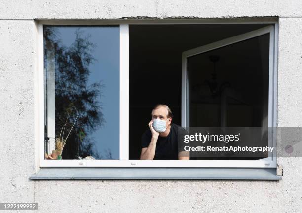 man wearing a face mask looking out of a window, lithuania - confinamiento fotografías e imágenes de stock