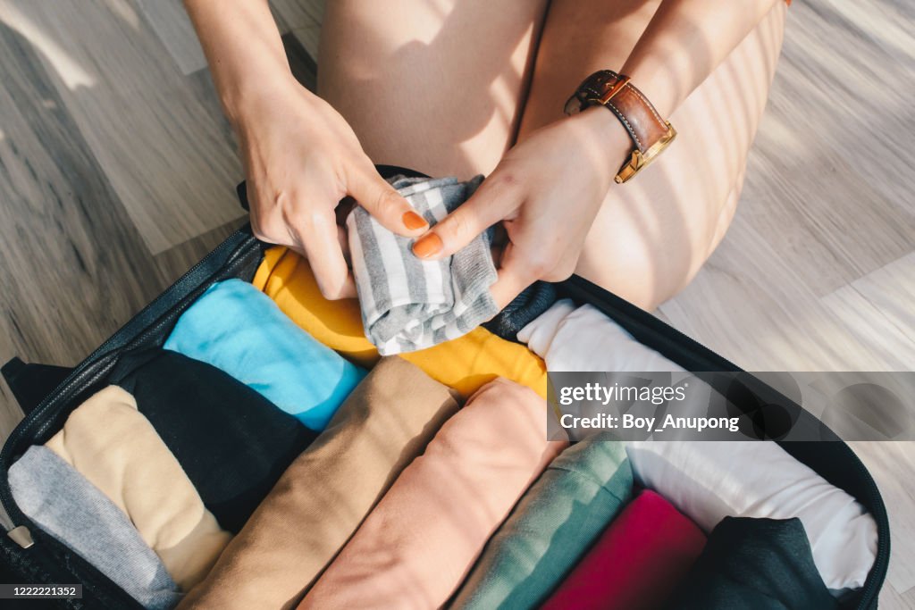 Close-up of tourist woman open suitcase roll and pack colorful cloths for travelling.