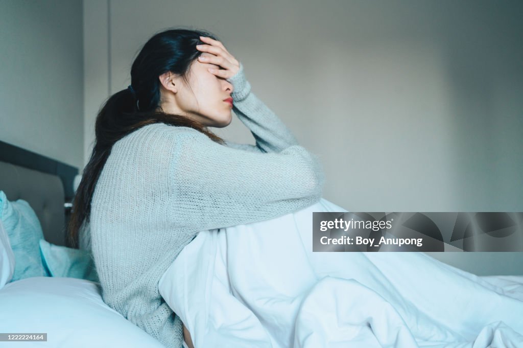 Portrait of sickness woman sitting alone on the bed in the bedroom, self isolation herself during coronavirus pandemic outbreak.
