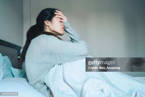 portrait of sickness woman sitting alone on the bed in the bedroom, self isolation herself during coronavirus pandemic outbreak. - illness stock-fotos und bilder