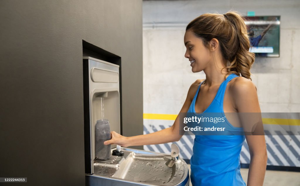 Vrouw bij de gymnastiek die haar waterfles vult