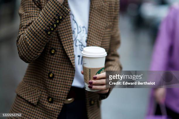Guest wears a brown jacket, holds a Starbucks coffee cup, during London Fashion Week Fall Winter 2020 on February 16, 2020 in London, England.