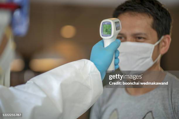 doctor man use infrared forehead thermometer gun to check body temperature for virus covid-19 symptoms with the isolation gown or protective suits and surgical face masks - temperature checkpoint stock pictures, royalty-free photos & images