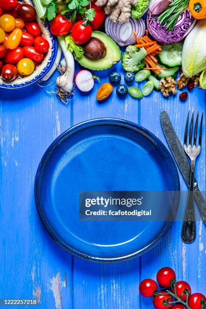 vegan food: empty blue plate and healthy fresh vegetables border. copy space - blue plate stock pictures, royalty-free photos & images