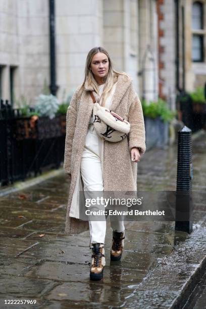 Nina Suess wears a fluffy faux fur coat, a fluffy Vuitton fanny pack bag, white pants, boots, during London Fashion Week Fall Winter 2020 on February...