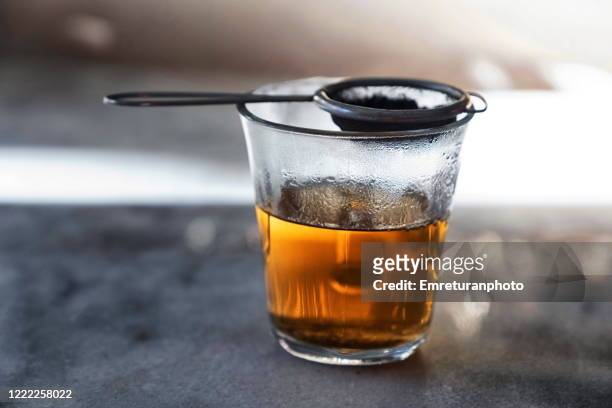 glass filled with hot tea from a strainer filled with tea leaves on top on a gray marble tabletop. - tè nero foto e immagini stock