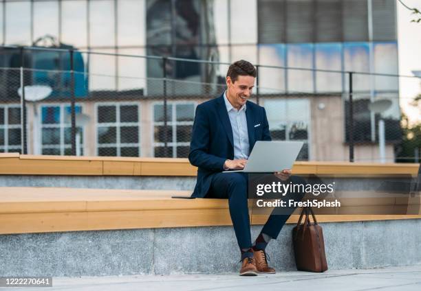 business on the go: businessman working on his laptop on the street - blue suit stock pictures, royalty-free photos & images