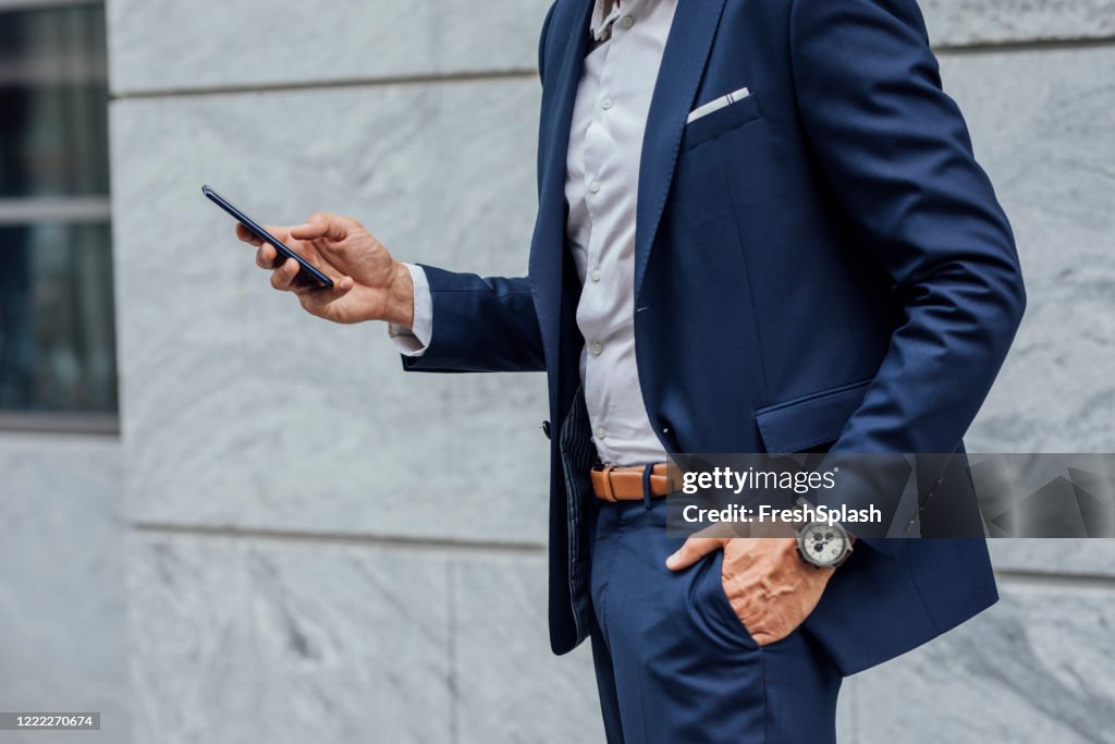 Connected on the Go: Hands of an Unrecognizable Businessman Using his Mobile Phone on the Street