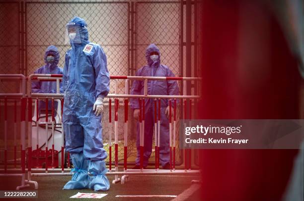 Chinese epidemic control workers wear protective suits as they watch over an area where people were undergoing nucleic acid swab tests for COVID-19...