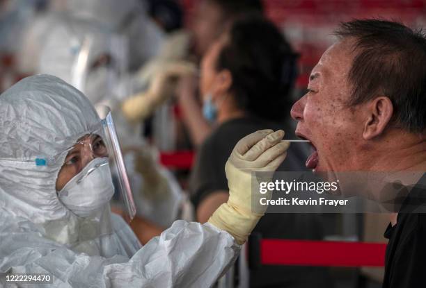 Chinese epidemic control worker wears a protective suit as she performs a nucleic acid swab test for COVID-19 on a man at a government testing site...