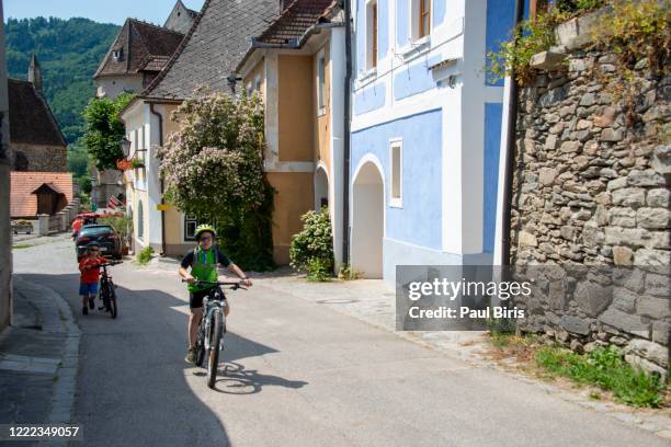 cute little kids biking on the streets of weißenkirchen in der wachau town, austria - 下奧地利州 個照片及圖片檔