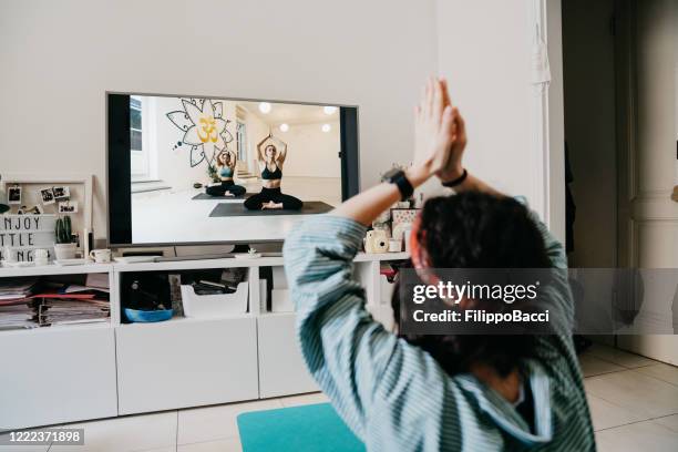 woman practicing yoga at home with a video lesson on the tv - net sports equipment stock pictures, royalty-free photos & images