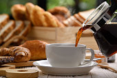 Pouring coffee with smoke on a cup with breads or bun, croissant and bakery on white wooden table