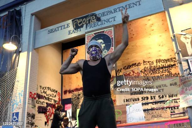 Man wearing a facemask flashes a hand sign defiantly in the air outside Seattle's abandoned East Precinct police station in the Capitol Hill Occupied...