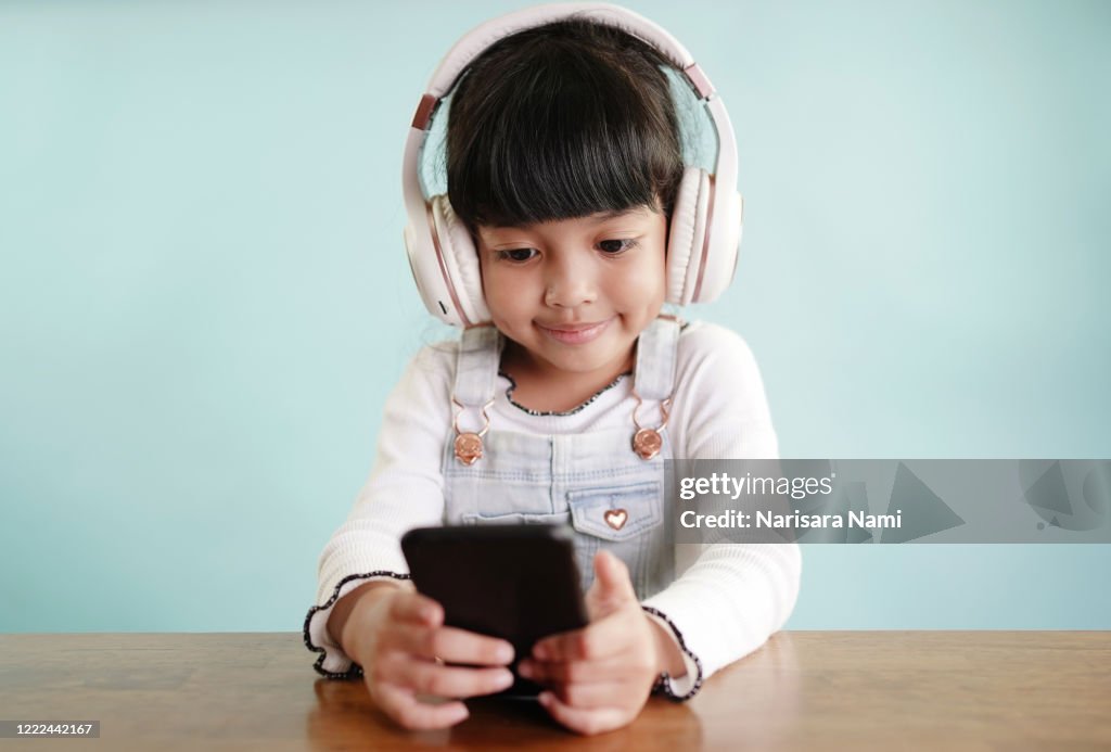 Happy asian cute child girl using mobile phone to open the music song from smartphone application. technology concept.