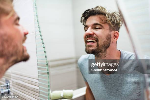 man looking at his face in the mirror - mirror imagens e fotografias de stock