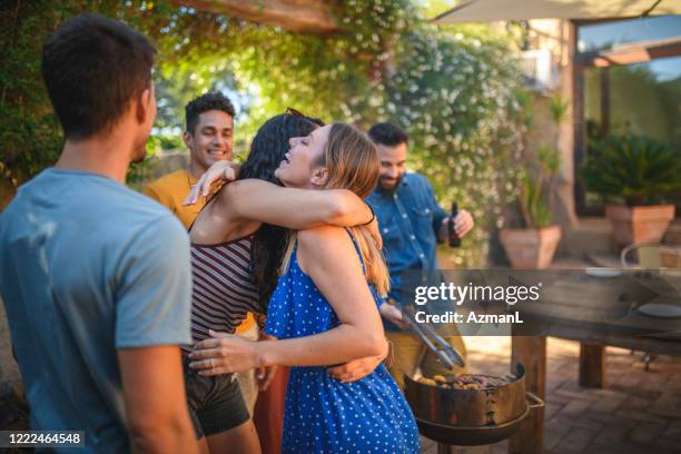 lachende vrouwelijke vrienden die bij openluchtbarbecuepartij koesteren - courtyard stockfoto's en -beelden