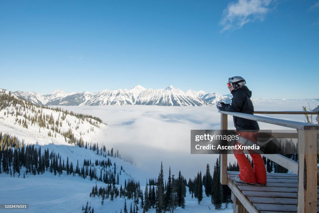 Alpine skier relaxes above fog bank, mountains and valley