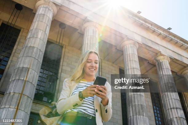 glimlachende blonde student van de wet met rugzak en slimme telefoon - greek independence day stockfoto's en -beelden