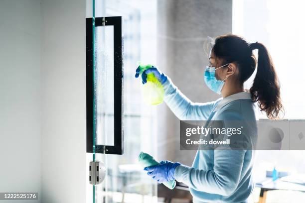 female wearing protective face mask cleaning home with disinfectant wipe - office cleaning stock pictures, royalty-free photos & images