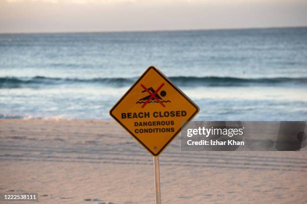 a sign with the statement "beach closed" and the "no swimming" symbol is showed at bondi beach, sydney, new south wales, australia. - bondi beach sign stock pictures, royalty-free photos & images