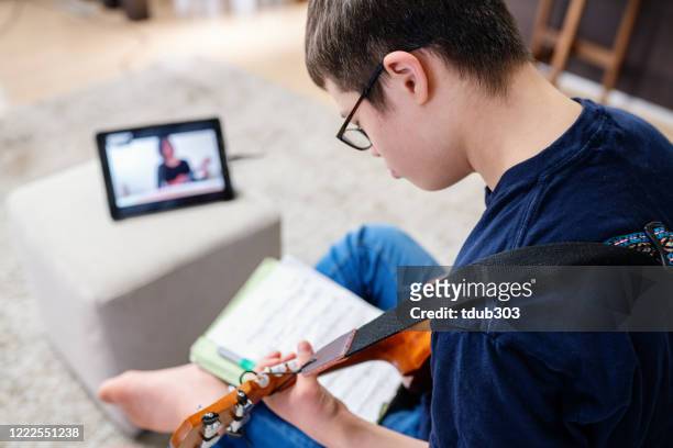 Teenage boy with Down' Syndrome taking distant learning music lessons at home over the internet