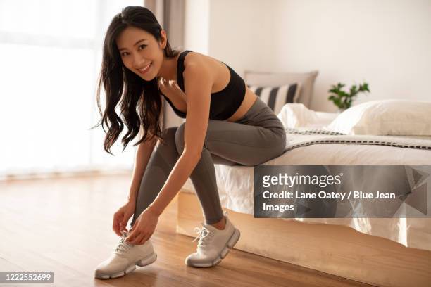 happy young chinese woman getting ready for morning exercise - junge frau bett sitzen blick in die kamera stock-fotos und bilder