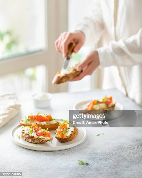 la donna fa bruschetta con salmone, cagliata e cetriolo su pane tostato in stile high key su sfondo bianco. - bruschetta foto e immagini stock