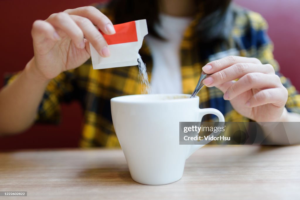 Young Asian woman pouring sugar into mug.