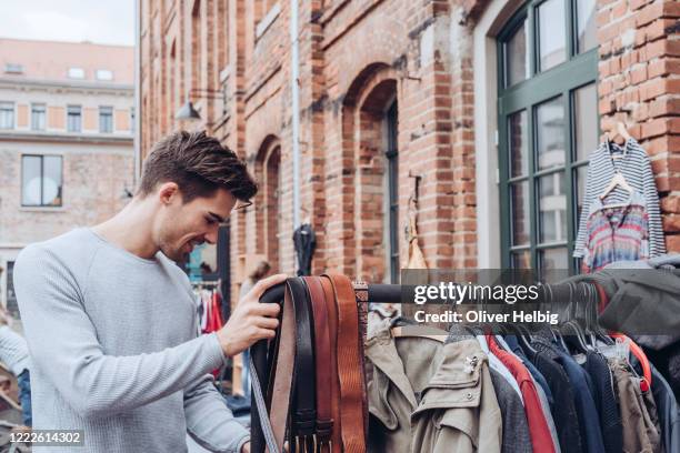 a handsome young adult man looking for second hand clothes at a flea market - flea market stockfoto's en -beelden