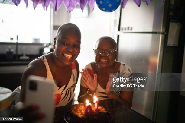 mother and daughter doing a video call on mobile phone celebrating birthday distance party - zoom birthday stock pictures, royalty-free photos & images
