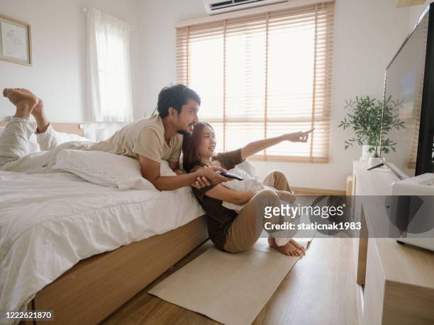 happy young asian couple watching tv together at home - smart tv stock pictures, royalty-free photos & images