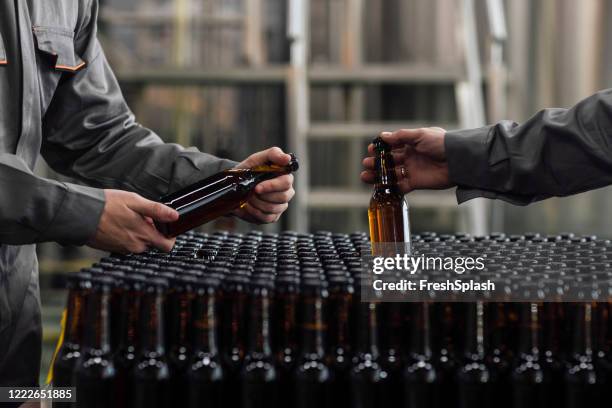 lager making process: onherkenbare fabrieksarbeiders holding gebotteld bier - beer bottles stockfoto's en -beelden