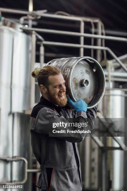 craft beer manufacturing: lächelnder brauereiarbeiter trägt bierfässer - bierfass stock-fotos und bilder