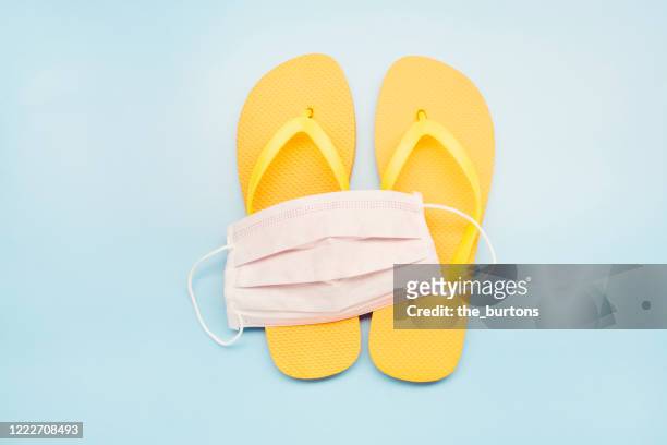 still life of a white face mask and orange flip-flops on blue background, on vacation with a protective face mask - vacances plage stock-fotos und bilder