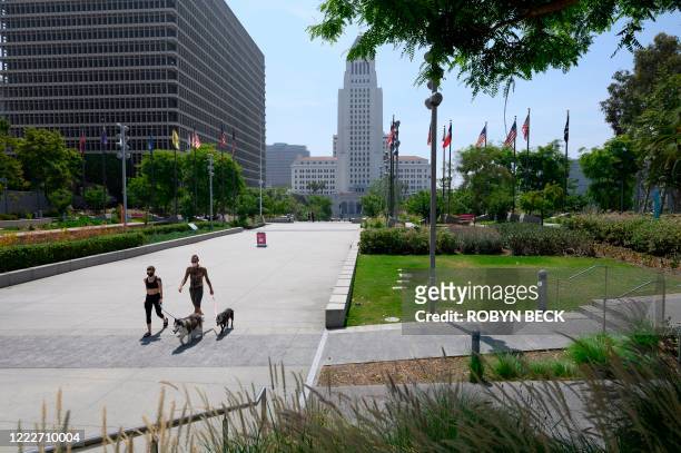 Man and woman wearing facemasks walk dogs in Grand Park with Los Angeles City Hall seen in the background, June 24, 2020 in Los Angeles, California...