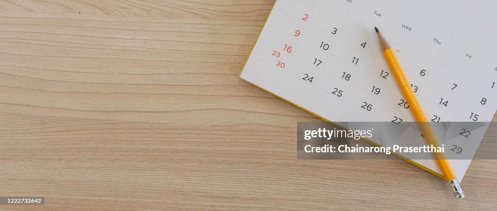 Close up top view on white calendar 2020 with yellow pencil and month schedule to make appointment meeting or manage timetable each day lay on wood table background for planning work and life