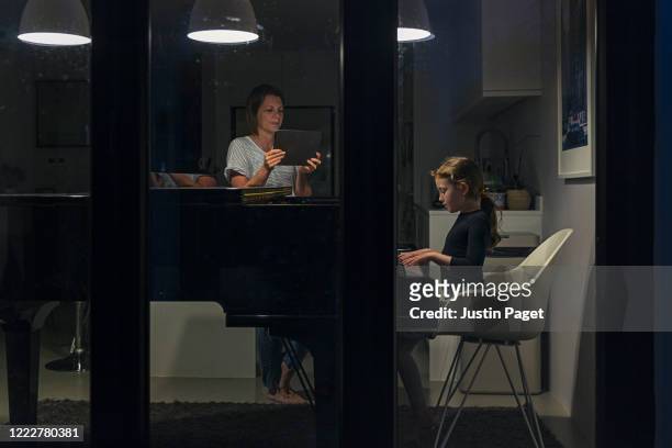 young girl playing piano. her mother is videoing her performance - photographed through window stock pictures, royalty-free photos & images