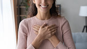 Close up happy sincere female holding folded hands on chest.