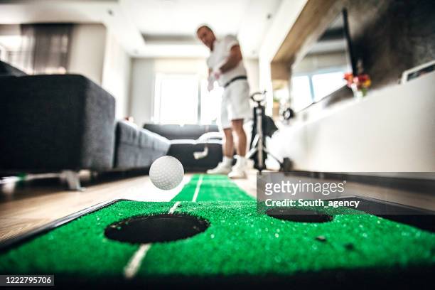 senior man playing mini golf in living room - indoor golf stock pictures, royalty-free photos & images