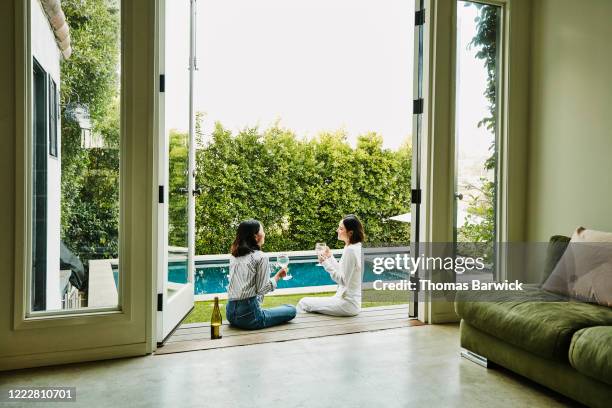 smiling friends sitting on deck overlooking backyard swimming pool sharing wine - backyard pool fotografías e imágenes de stock